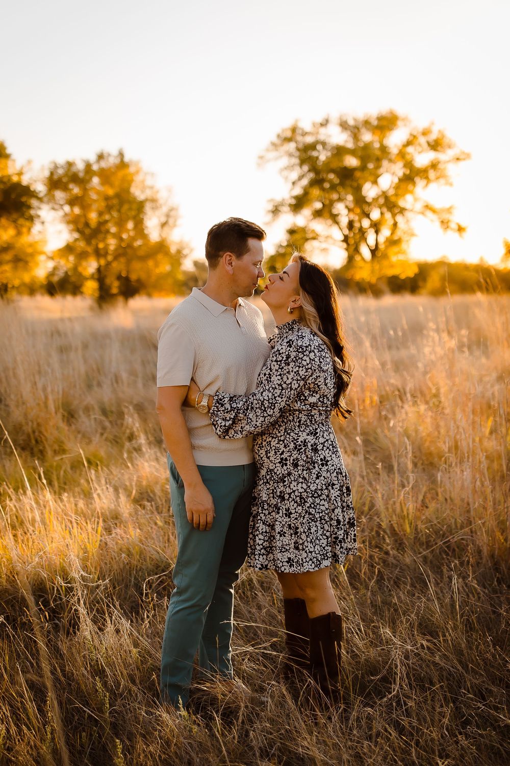 A couple smiles candidly at golden hour in a Denver grass field