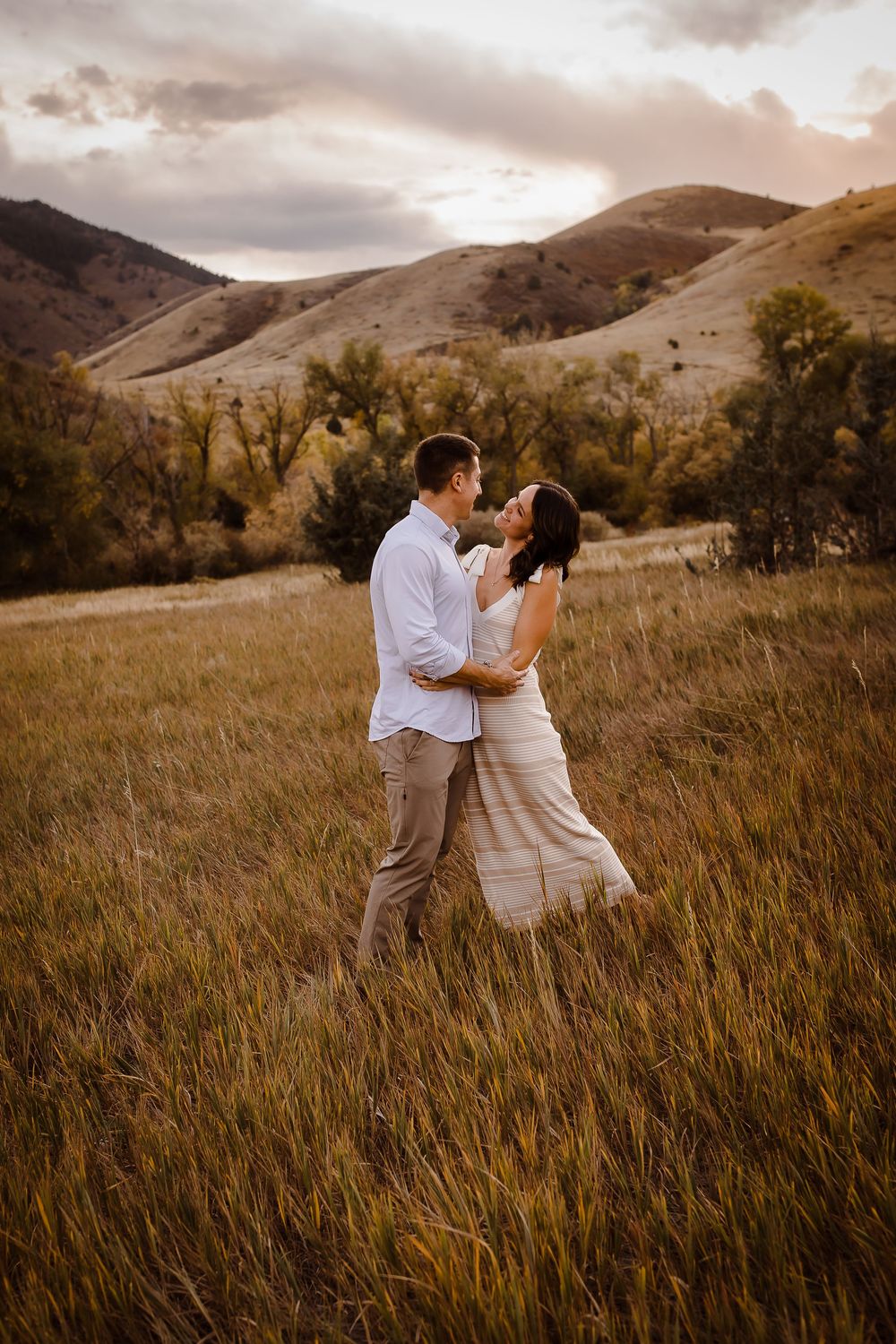 A couple naturally smiling standing in a grassy field in Morrison Colorado, Denver foothills