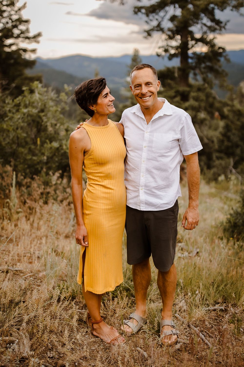 A couple smiles together in the Denver Colorado foothills with the mountains behind them