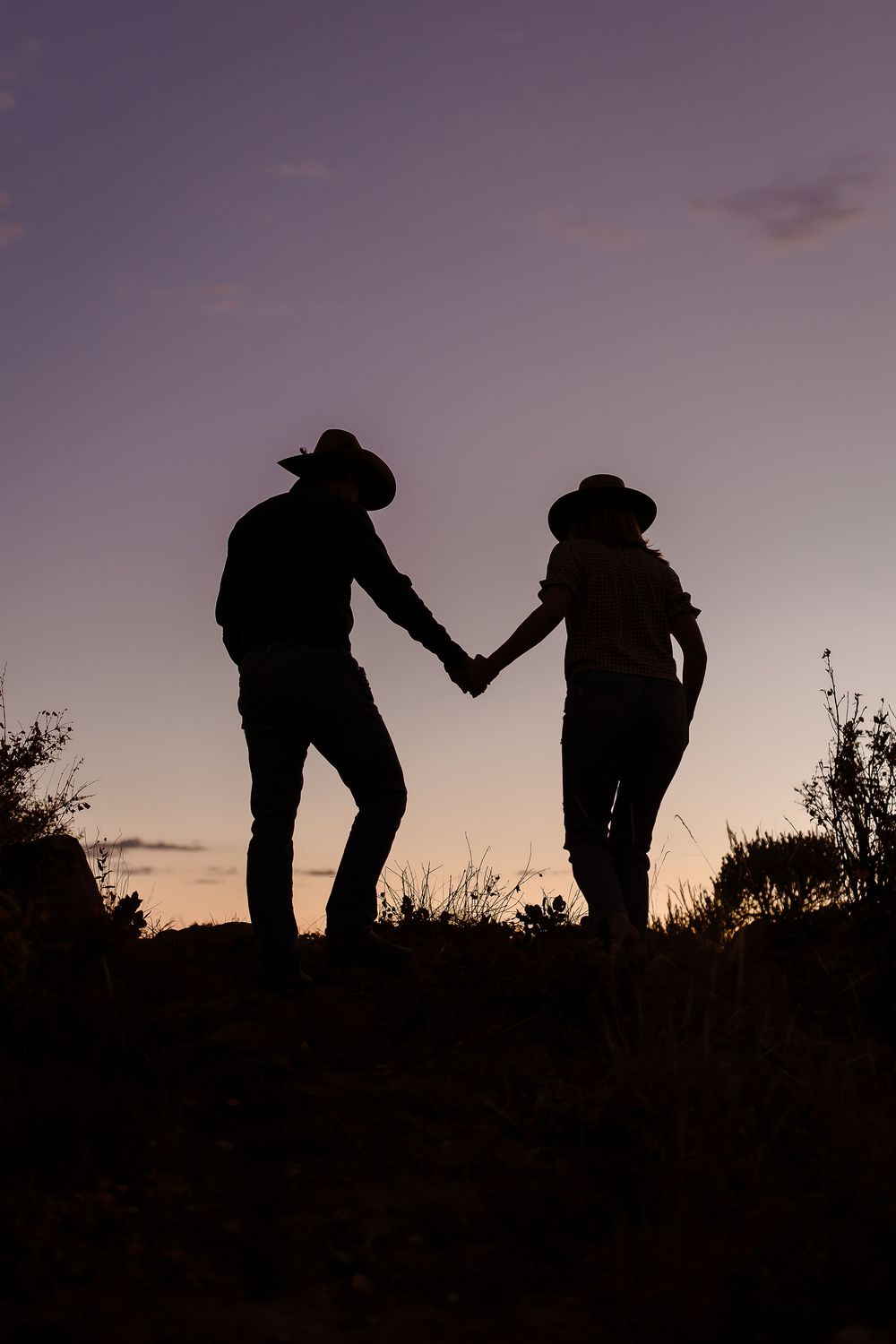 Silhouette of a couple in cowboy hats walking up a hill in front of a beautiful Colorado dusk sky