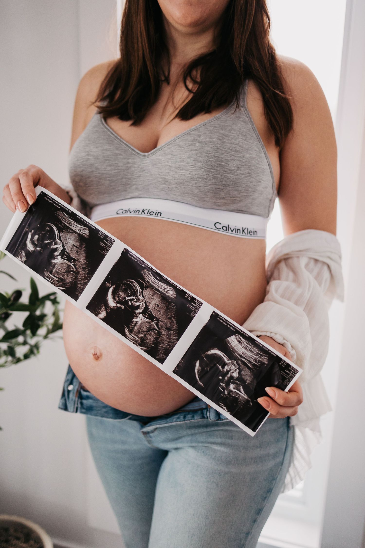 Expecting mother holding ultrasound photos while wearing casual attire.
