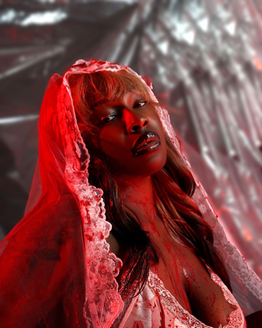 A woman in red lace veil and lingerie posed dramatically under intense red lighting with a metallic backdrop.