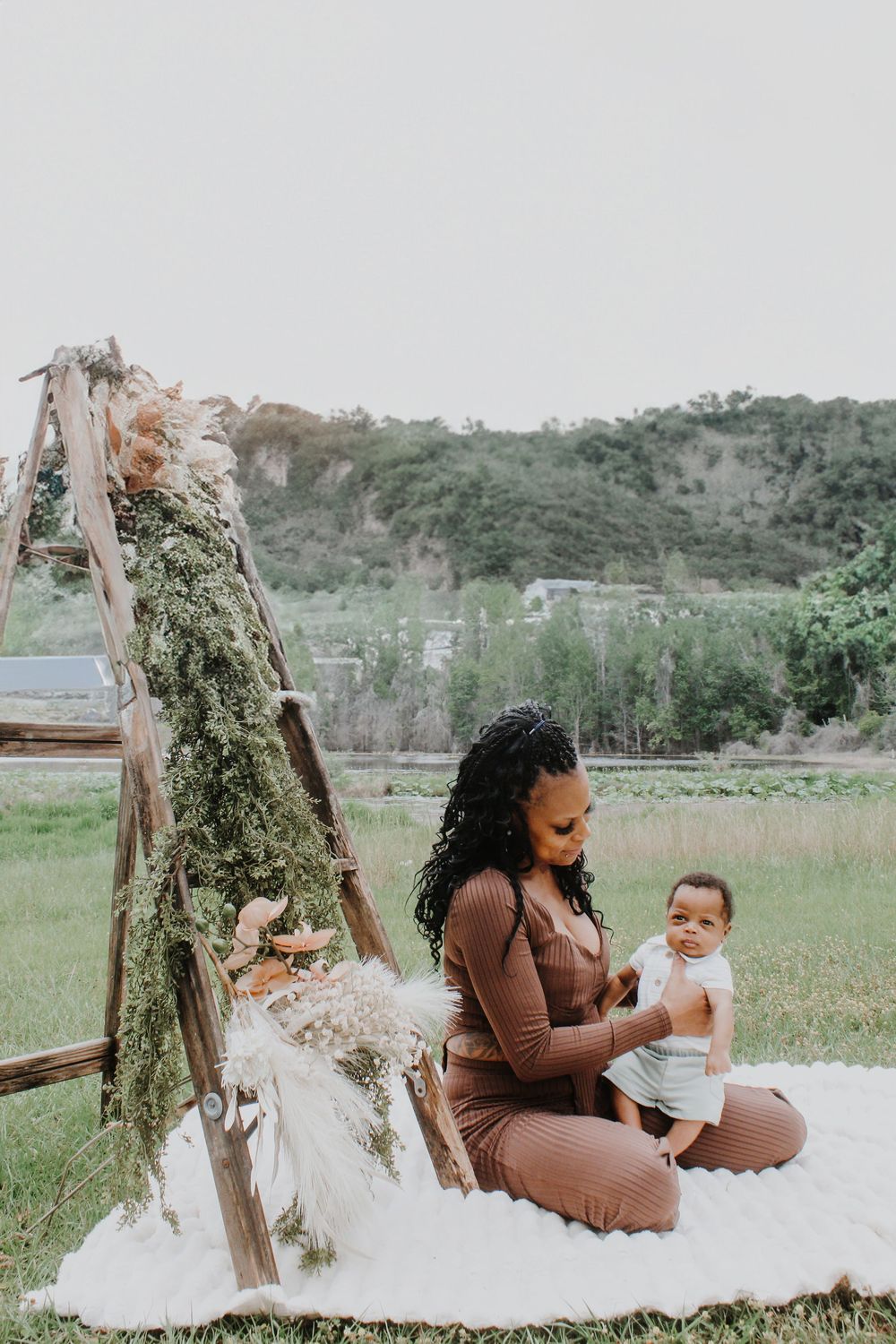 Outdoor photo setup with rustic ladder arch and blanket in natural setting.