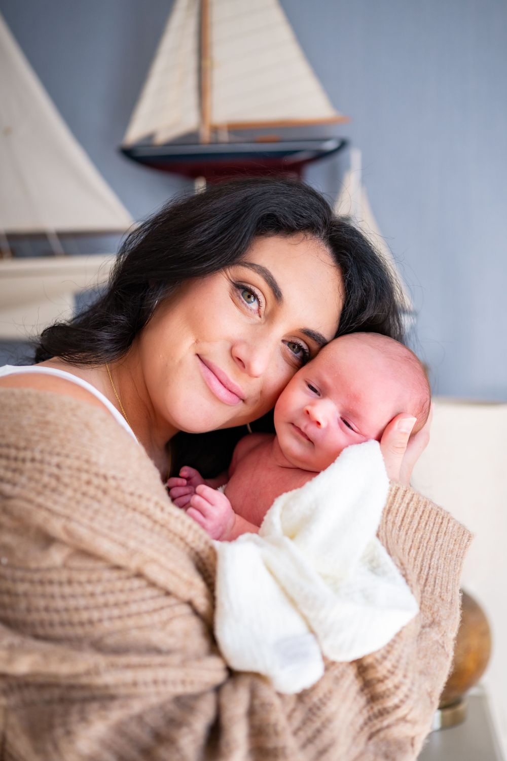 Loving portrait with newborn against wall decorated with model sailboats.