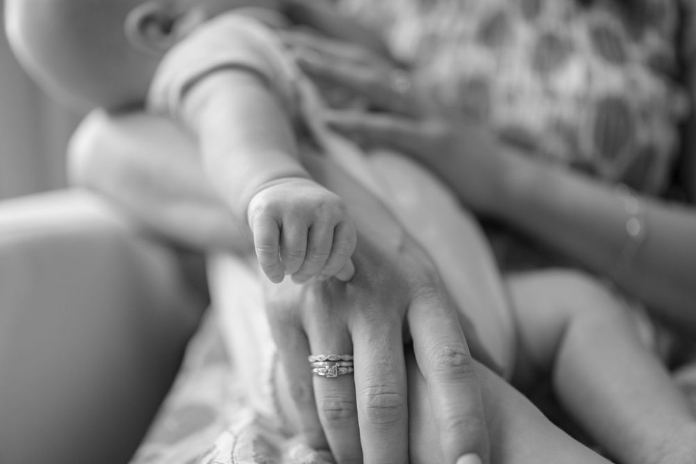 Black and white photo of a newborn baby grasping an adult finger wearing a wedding ring.