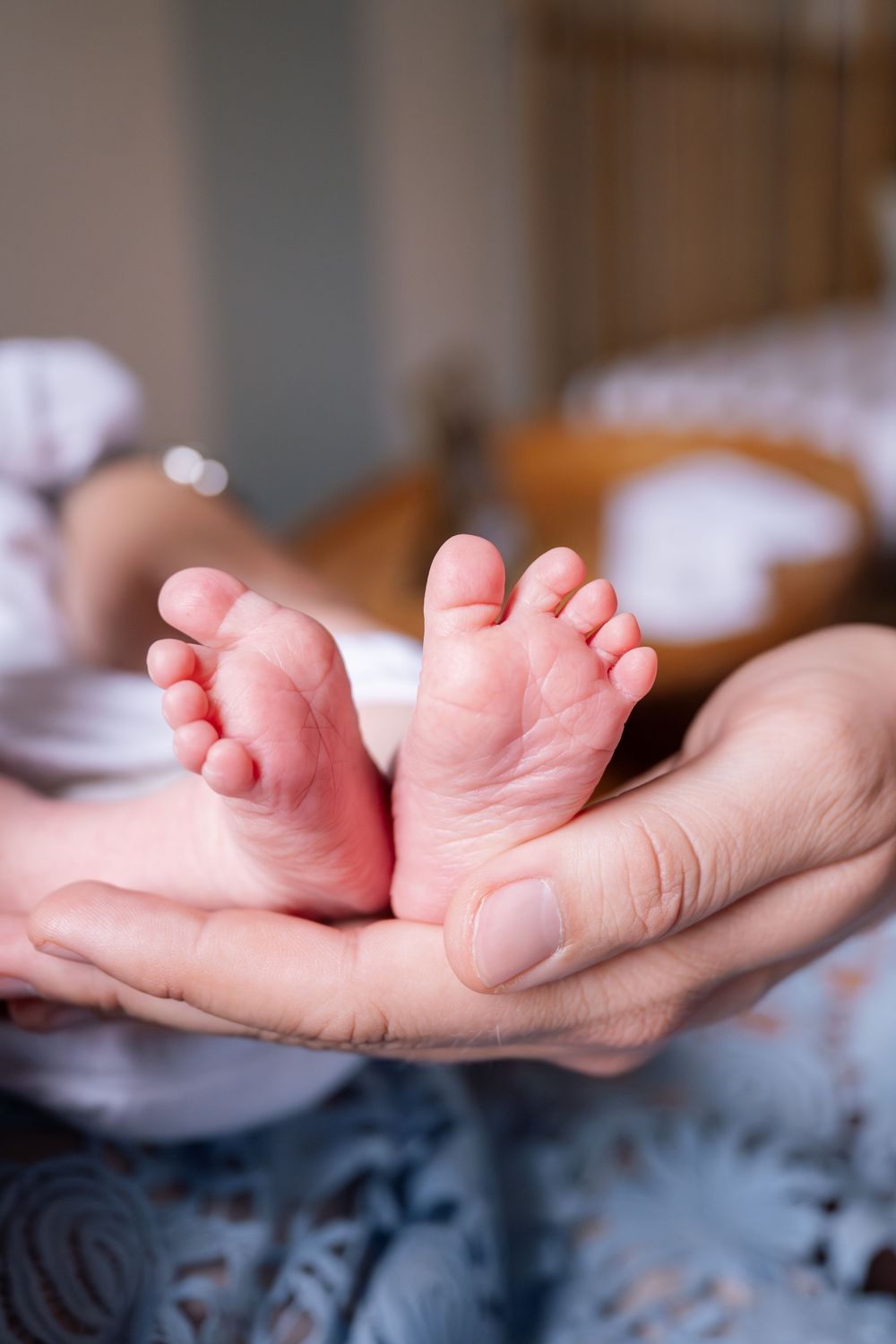 Tiny newborn baby feet resting in an adult's gentle cupping hands against a blue textured background.