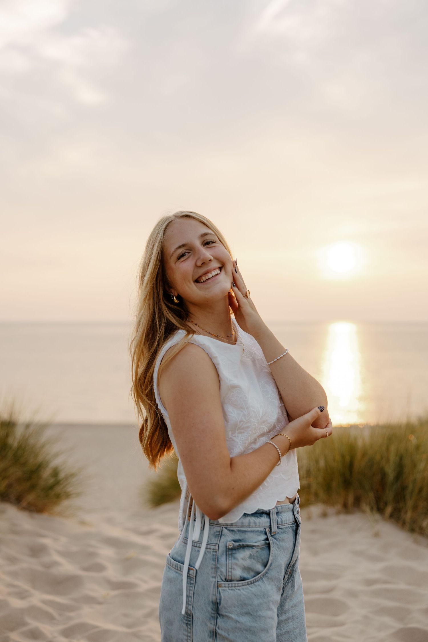 A young woman with long blonde hair smiles and poses on a beach with the ocean and sky in the background. Fort Worth Texas photographer