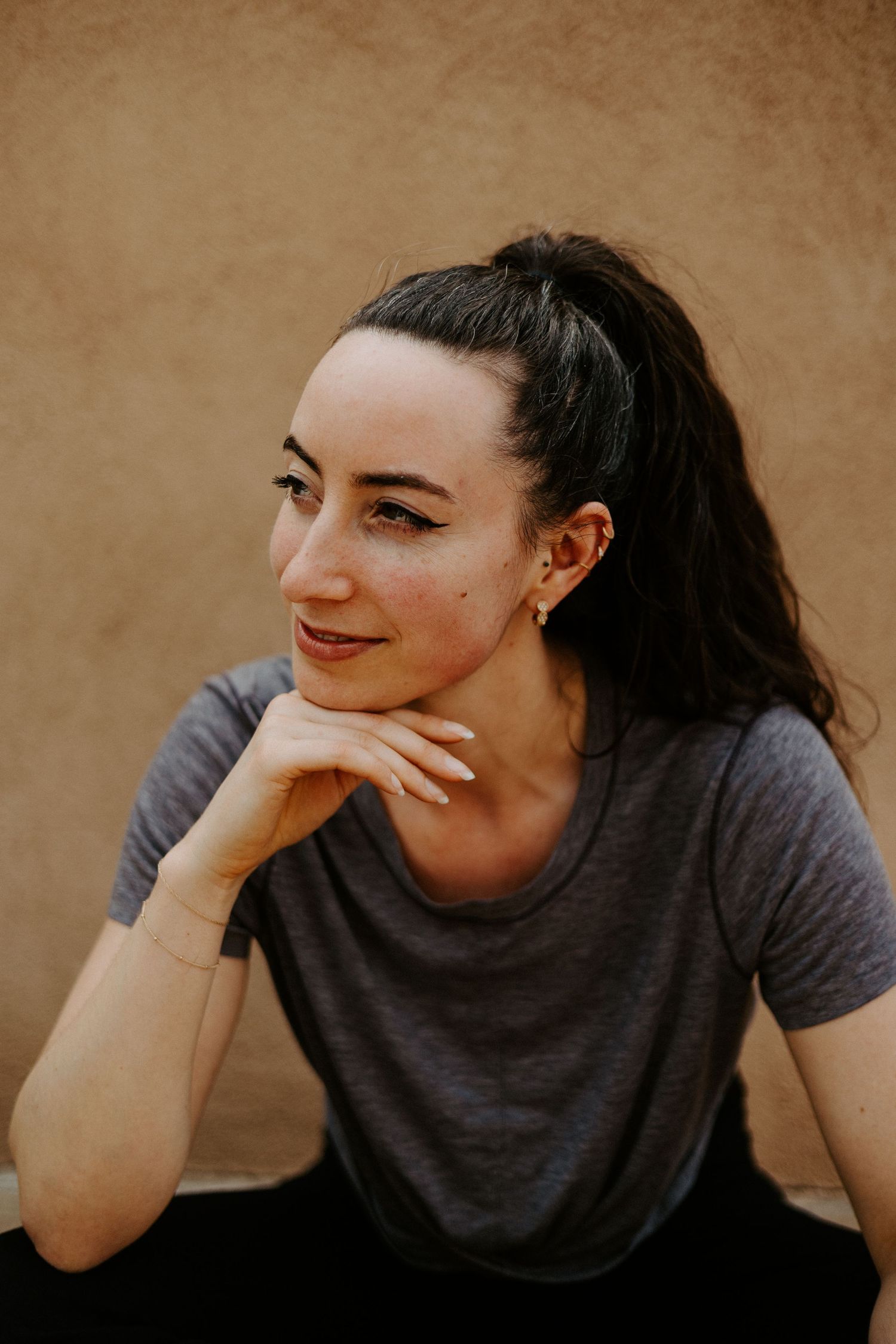 A casual portrait against a brown wall shows photographer wearing a gray t-shirt with dark hair and a warm smile.
