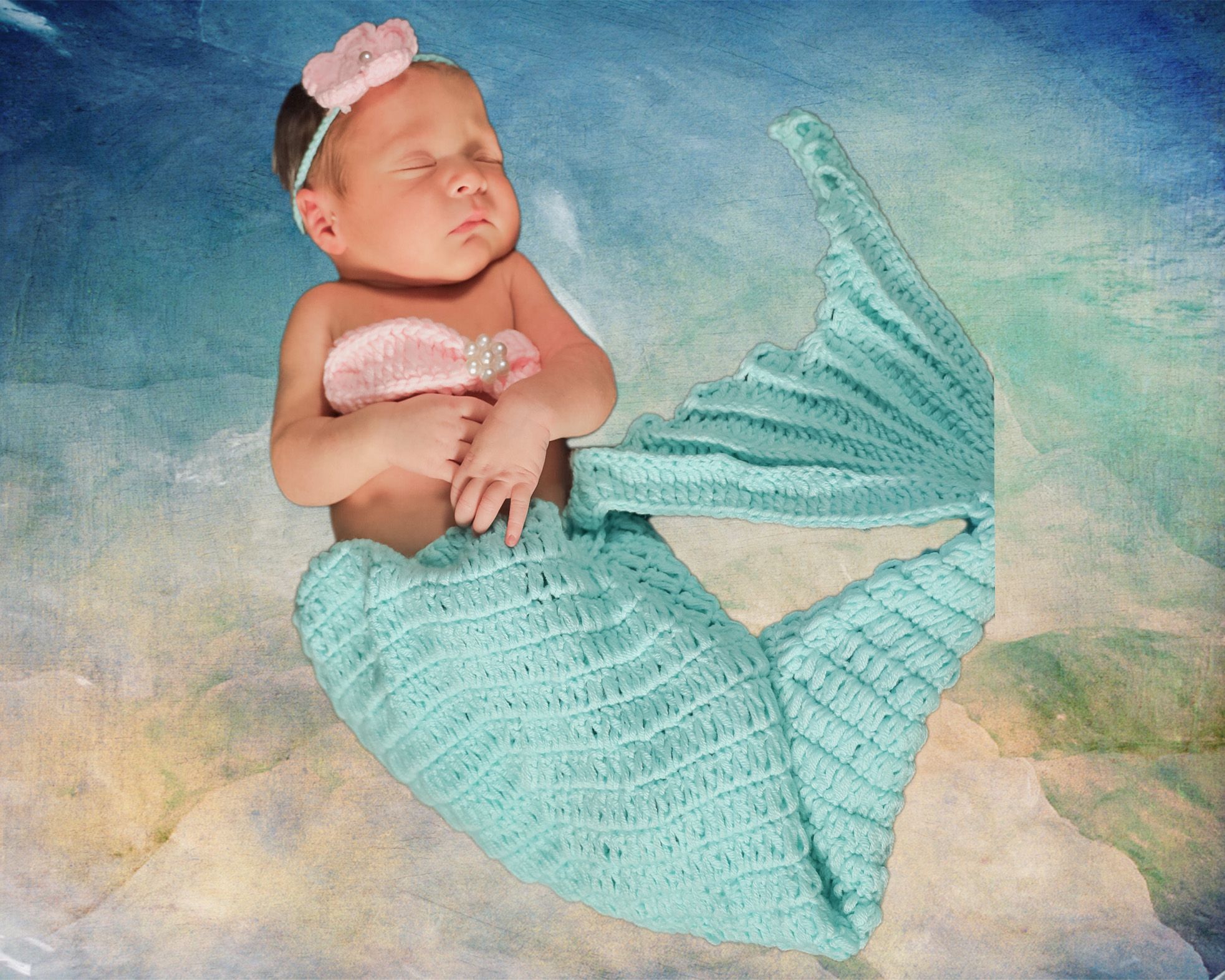 Newborn baby girl posed in crochet mermaid tail costume with pink flower headband.