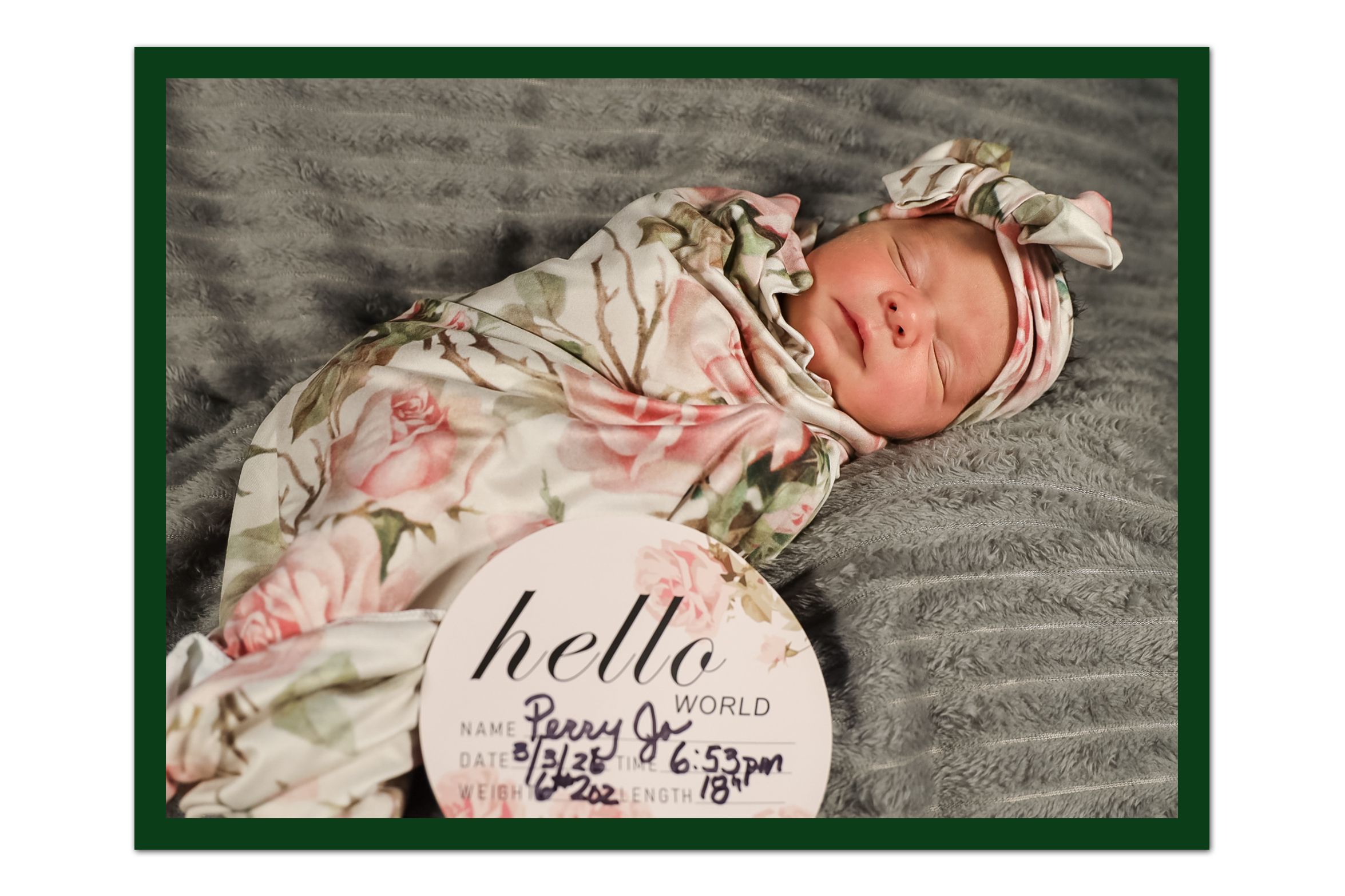 Newborn baby girl swaddled in floral blanket with pink headband beside a hello birth announcement sign.