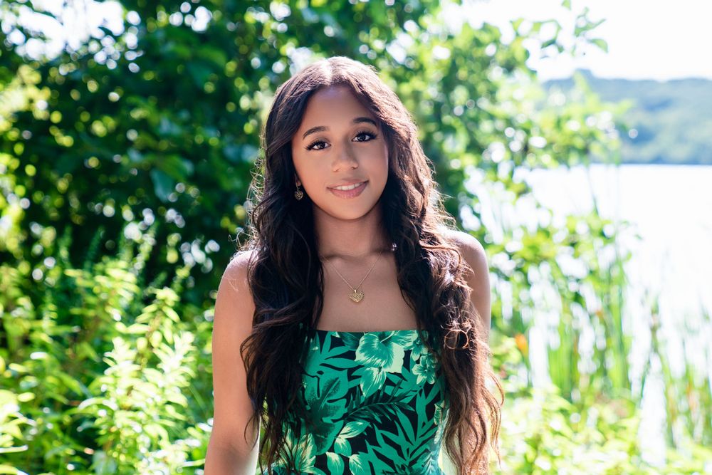 Portrait of person in green tropical print dress with water and foliage background.