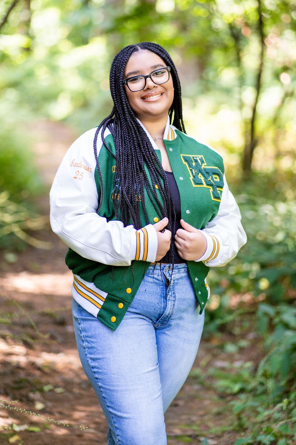 Portrait of person in varsity jacket and glasses on woodland path.