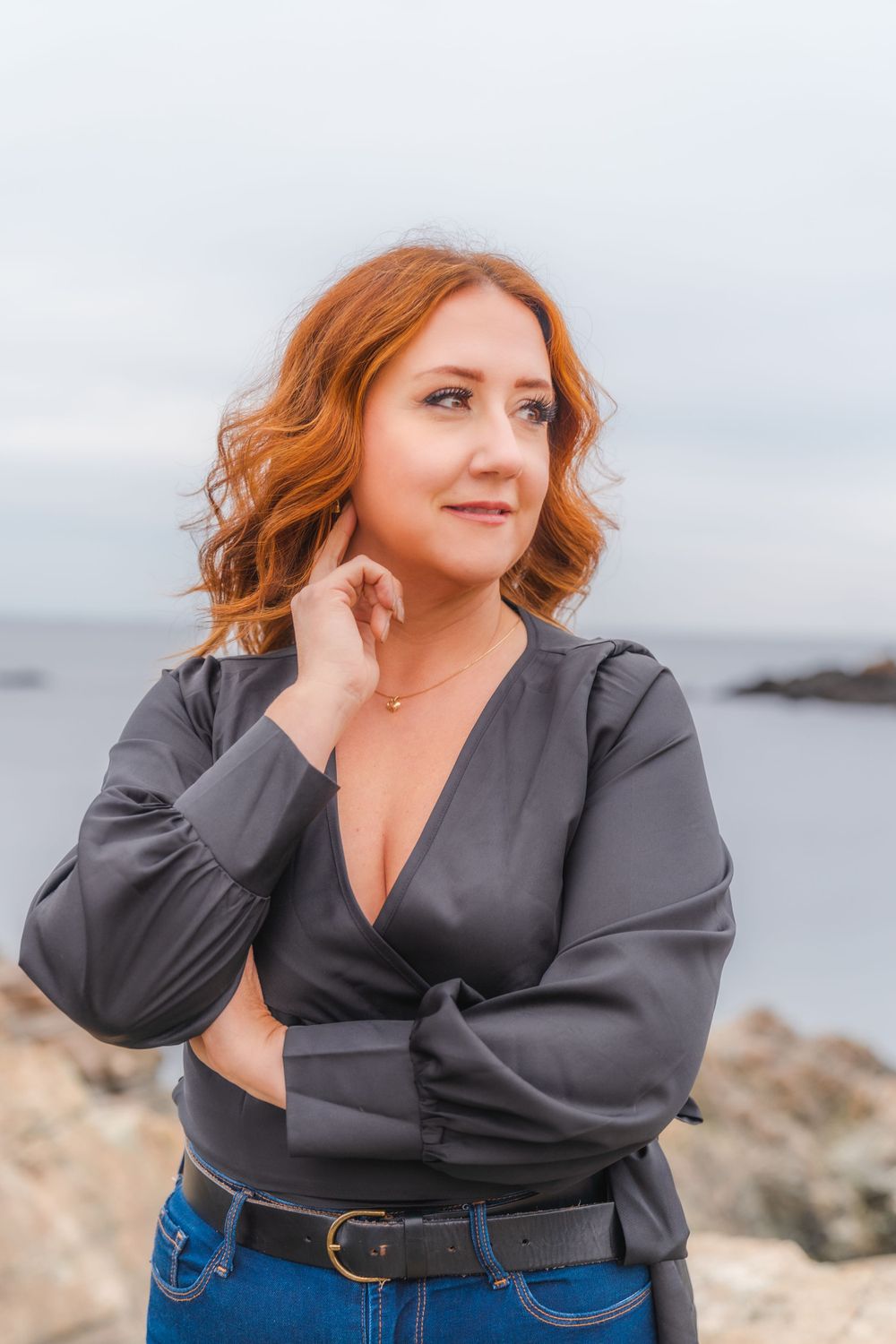 Portrait of person in black wrap top against coastal landscape.