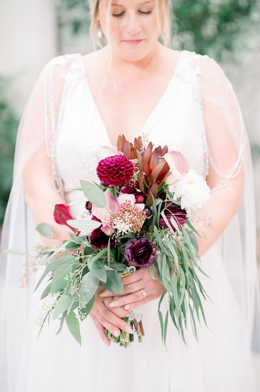 Elegant wedding bouquet featuring deep burgundy and pink flowers with cascading eucalyptus greenery against soft white dress.