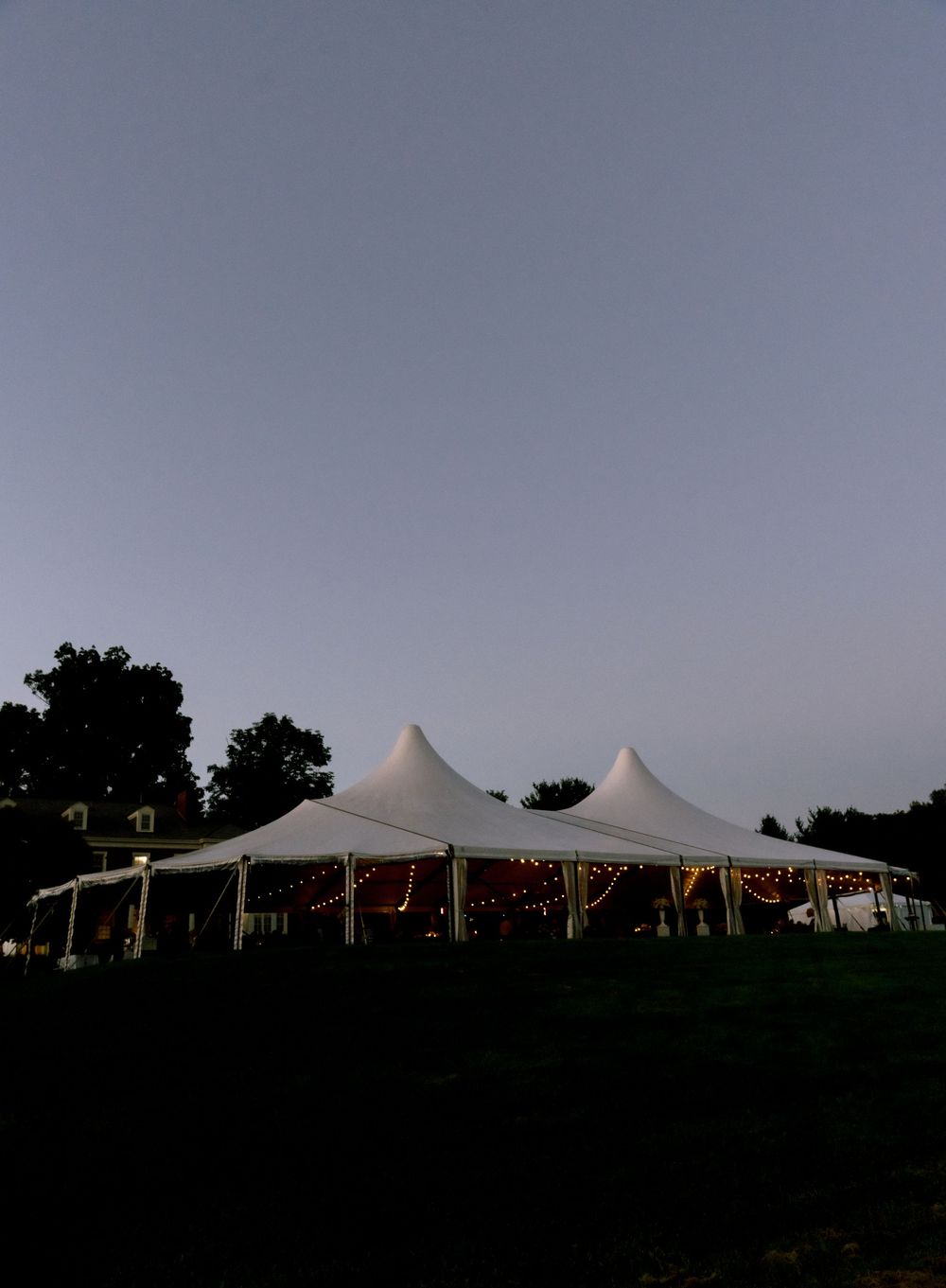 Illuminated white wedding tent glowing at dusk against twilight sky.