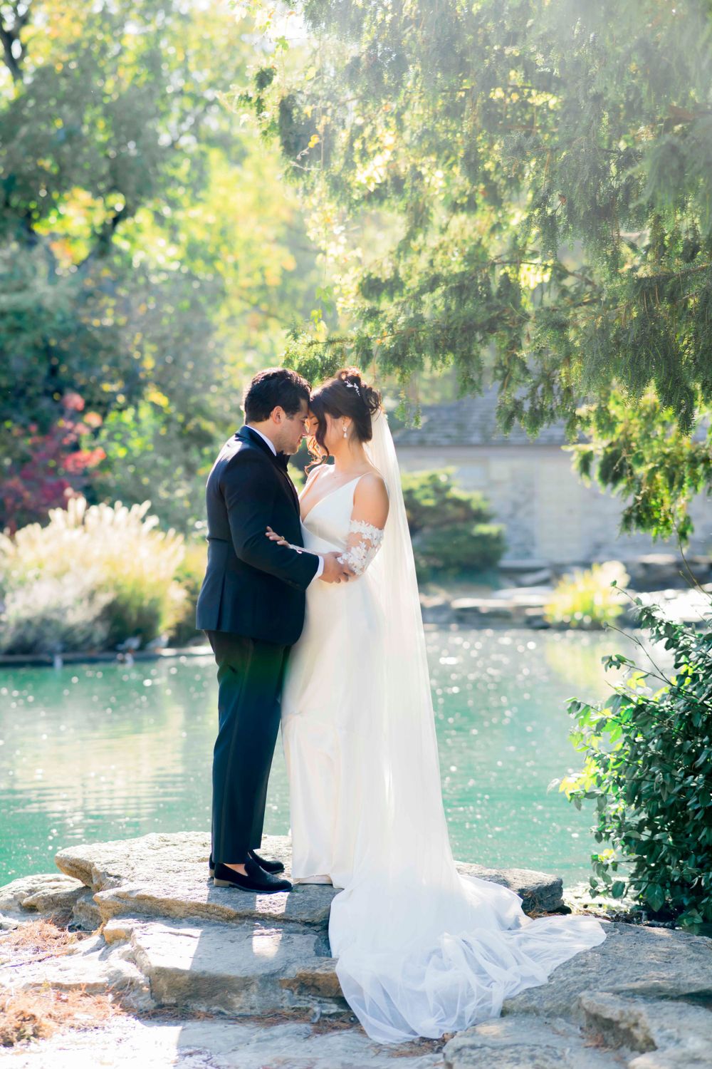 Romantic wedding moment captured by a serene pond with lush greenery.