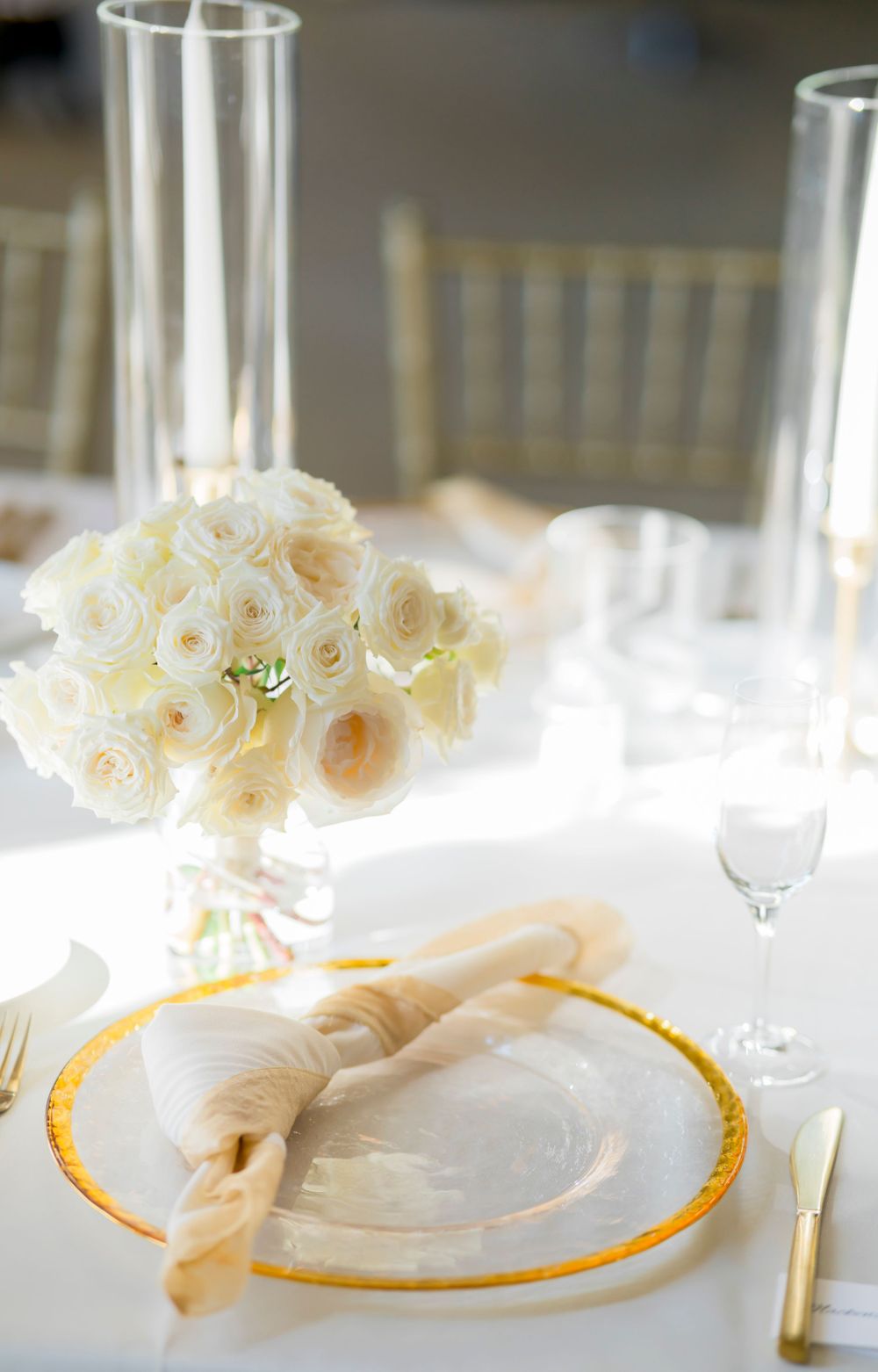 Elegant table setting with cream roses in a vase, gold-rimmed plates, and crystal champagne flutes.