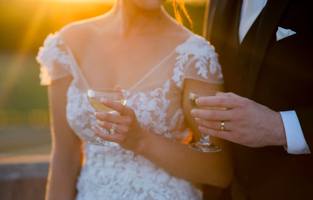 Wedding toast captured at golden hour with champagne glasses and lace dress details.