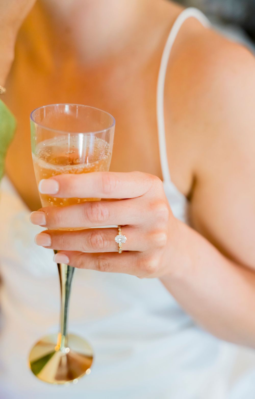 Close-up of a champagne glass being held with an engagement ring visible on the hand.