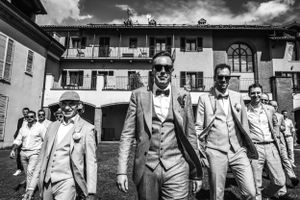 Zwart-witfoto van een zelfverzekerde bruidegom en zijn entourage in stijlvolle pakken, wandelend voor een Italiaanse villa