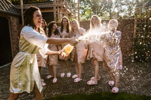 Bruidsmeisjes in satijnen kamerjassen vieren feest terwijl de bruid een fles champagne opent, met bruisende energie en sprankelende druppels