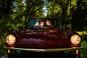 Romantisch bruidspaar in een klassieke rode cabrio, genietend van een intiem moment te midden van een sfeervol bosrijk decor