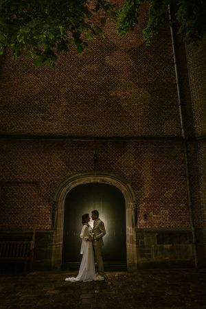 Bruidspaar in avondlicht bij kerkdeur in Willemstad, Nederland, gefotografeerd door Bart Boodts, huwelijksfotograaf Benelux