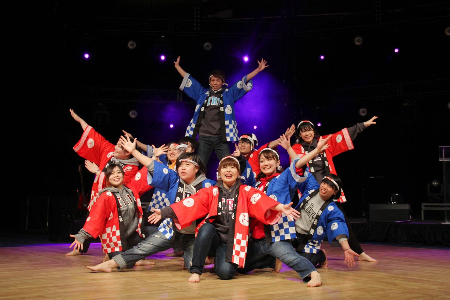 Energetic dance performance with group in red and blue costumes on stage with dramatic lighting.
