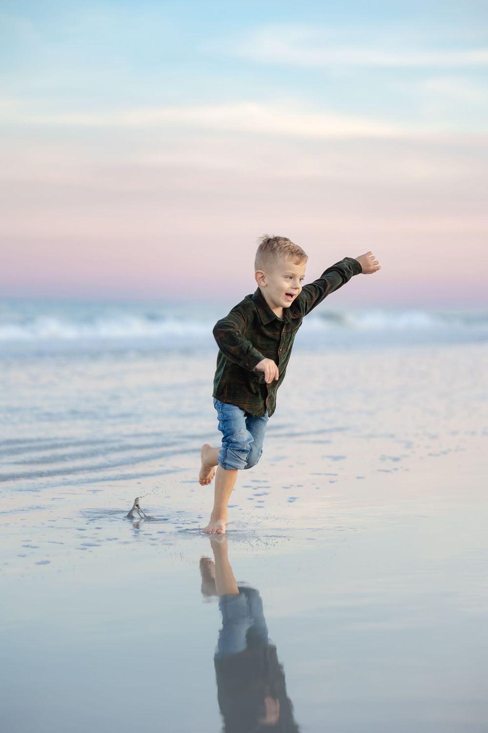 Child playing and jumping on wet beach sand during sunset.