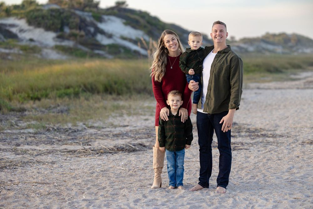 Happy family group poses together on coastal sand dunes at sunset.