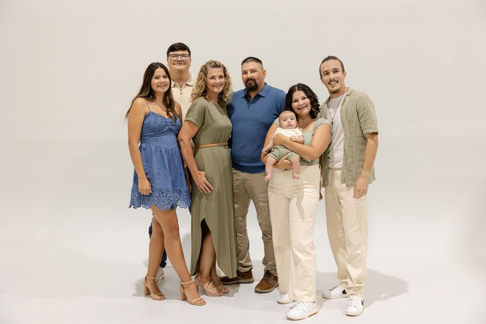 Family wearing coordinated neutral outfits poses together against white background for professional studio photos.