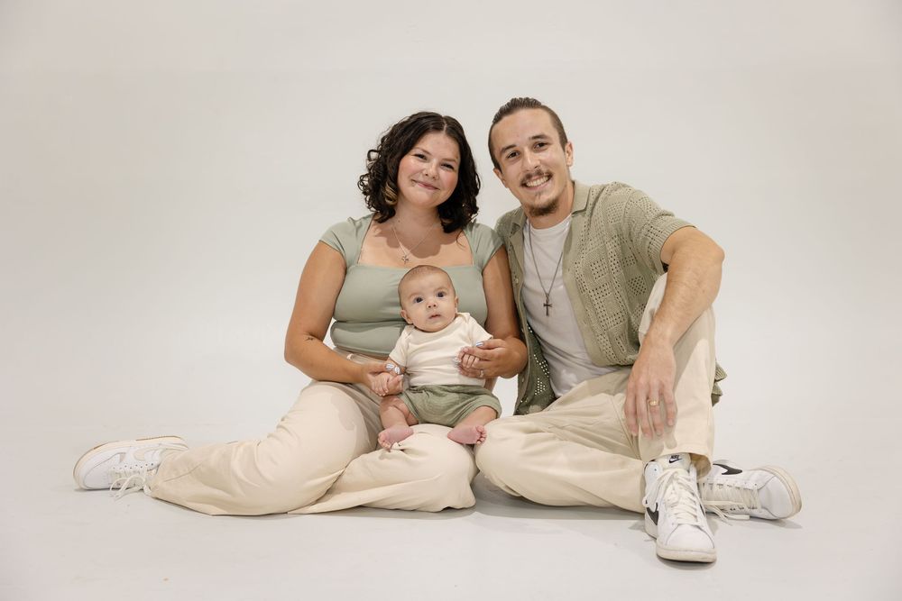 Family in neutral colored clothing poses on white background with baby for professional portraits.