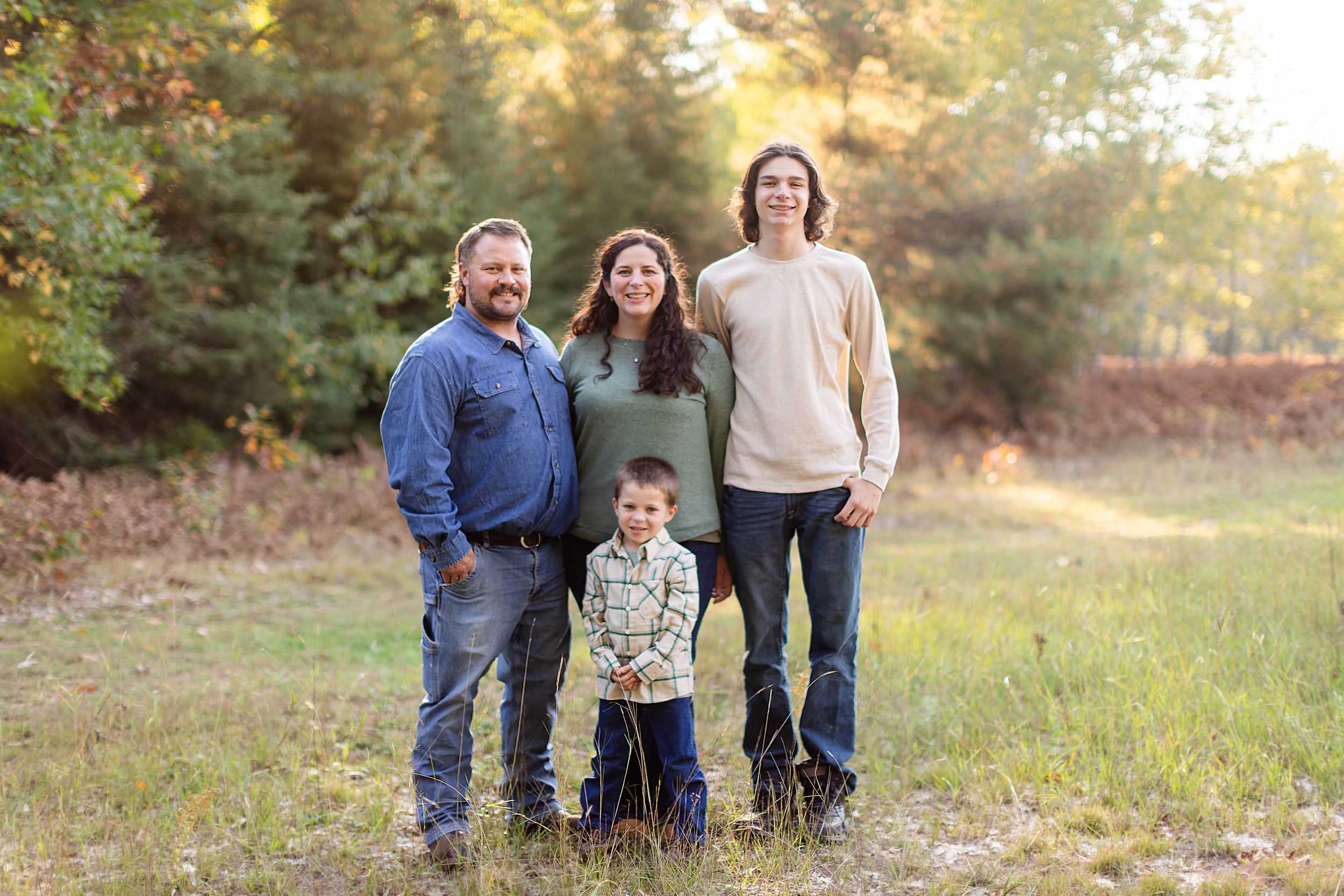 Family and dog pose together in a golden sunlit field during autumn sunset.