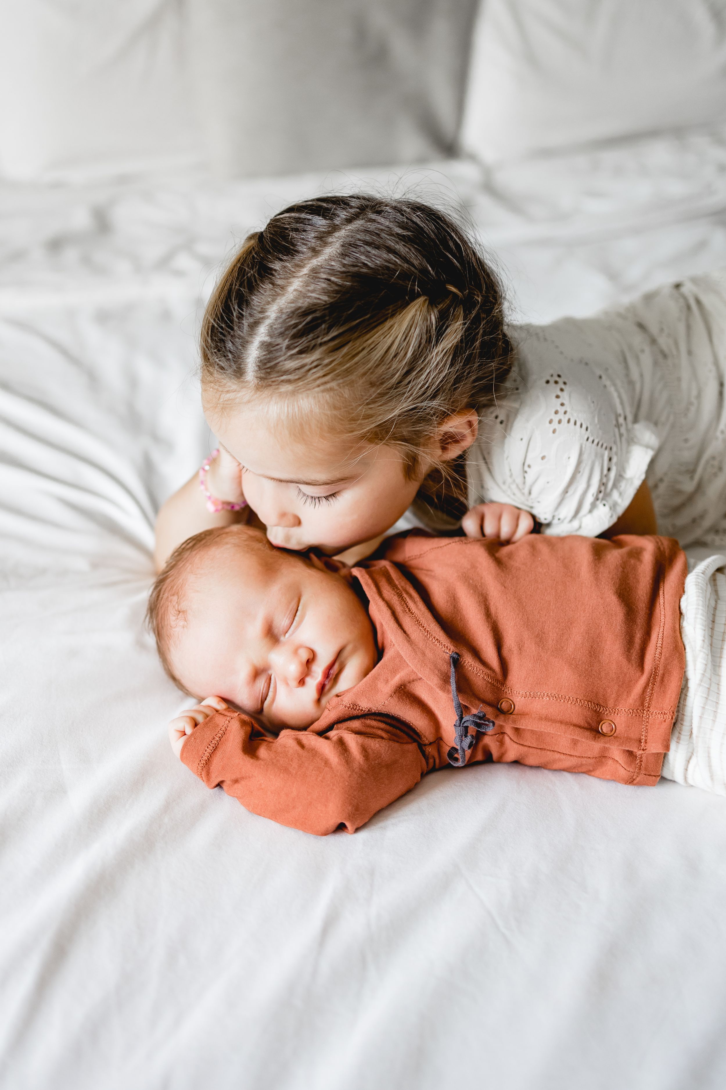 Child sleeping peacefully in a coral sweater on white bedding.