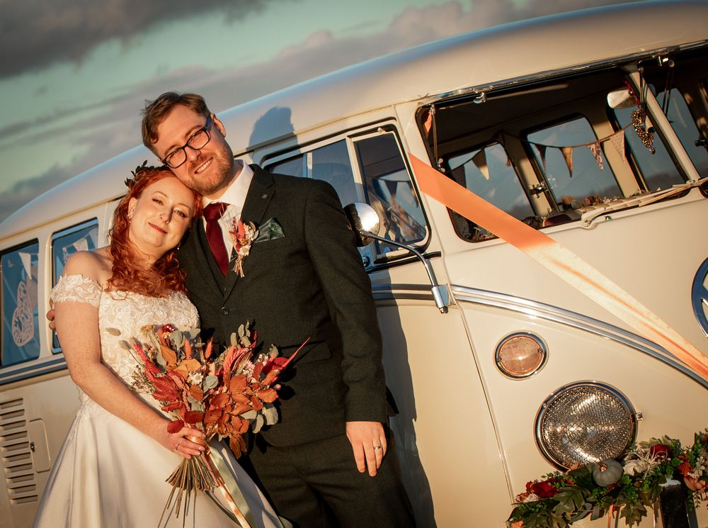 A vintage VW camper is the backdrop for a wedding couple at sunset with warm autumn-coloured florals. Shot at Notley Tythe Barn in Oxford