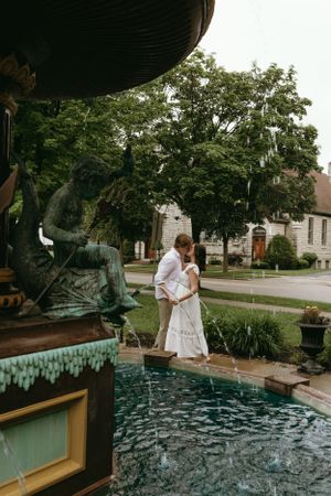 A couple sharing an intimate moment by a decorative fountain in a garden setting.