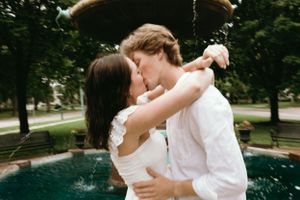 A romantic kiss by a fountain surrounded by lush greenery on a summer day.