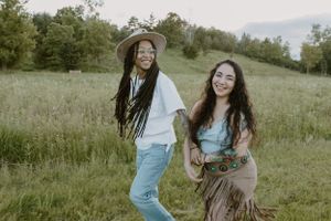 Two friends dance and laugh together in a grassy summer field.