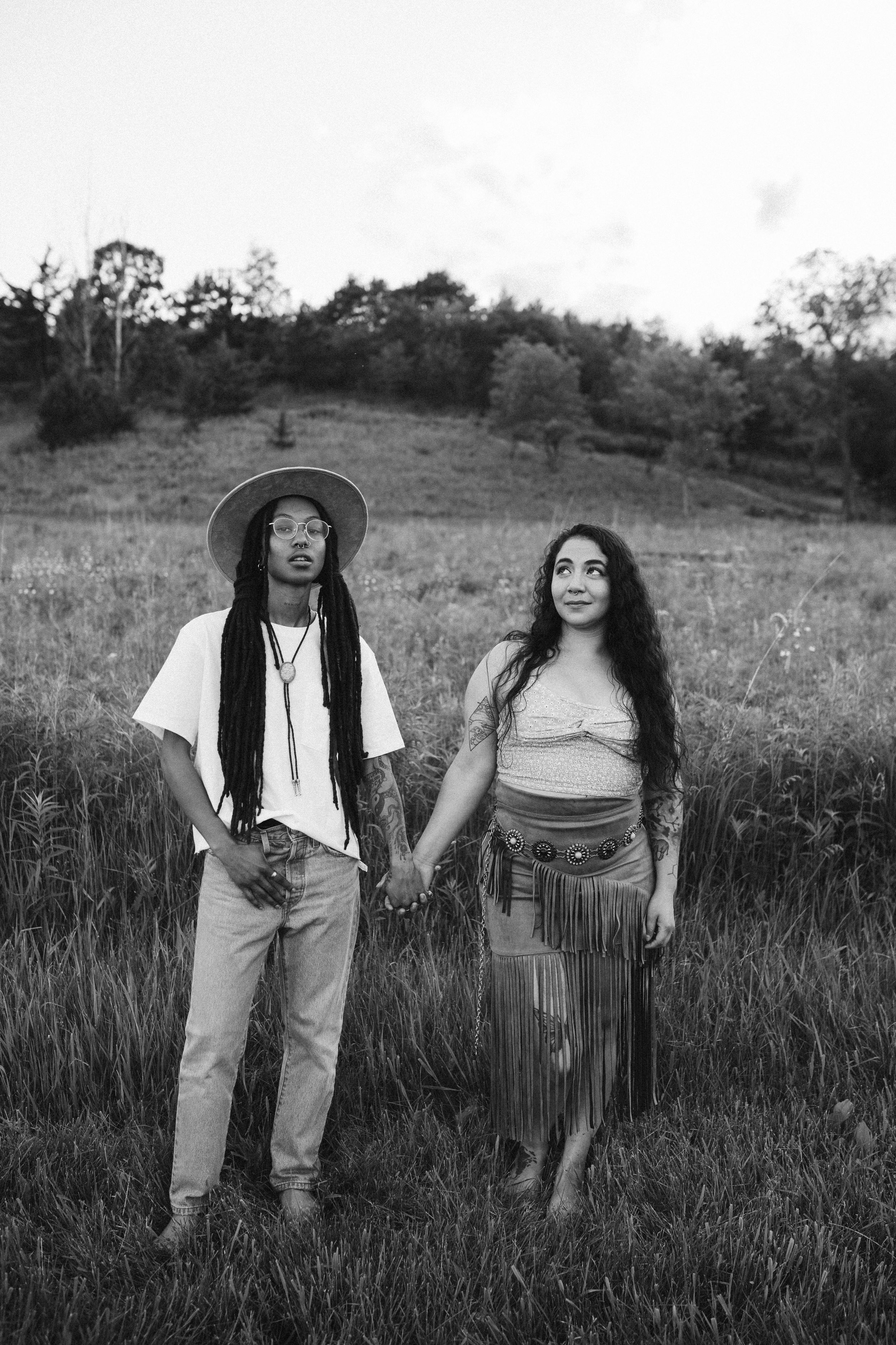 Black and white portrait of two friends holding hands in a wildflower field.