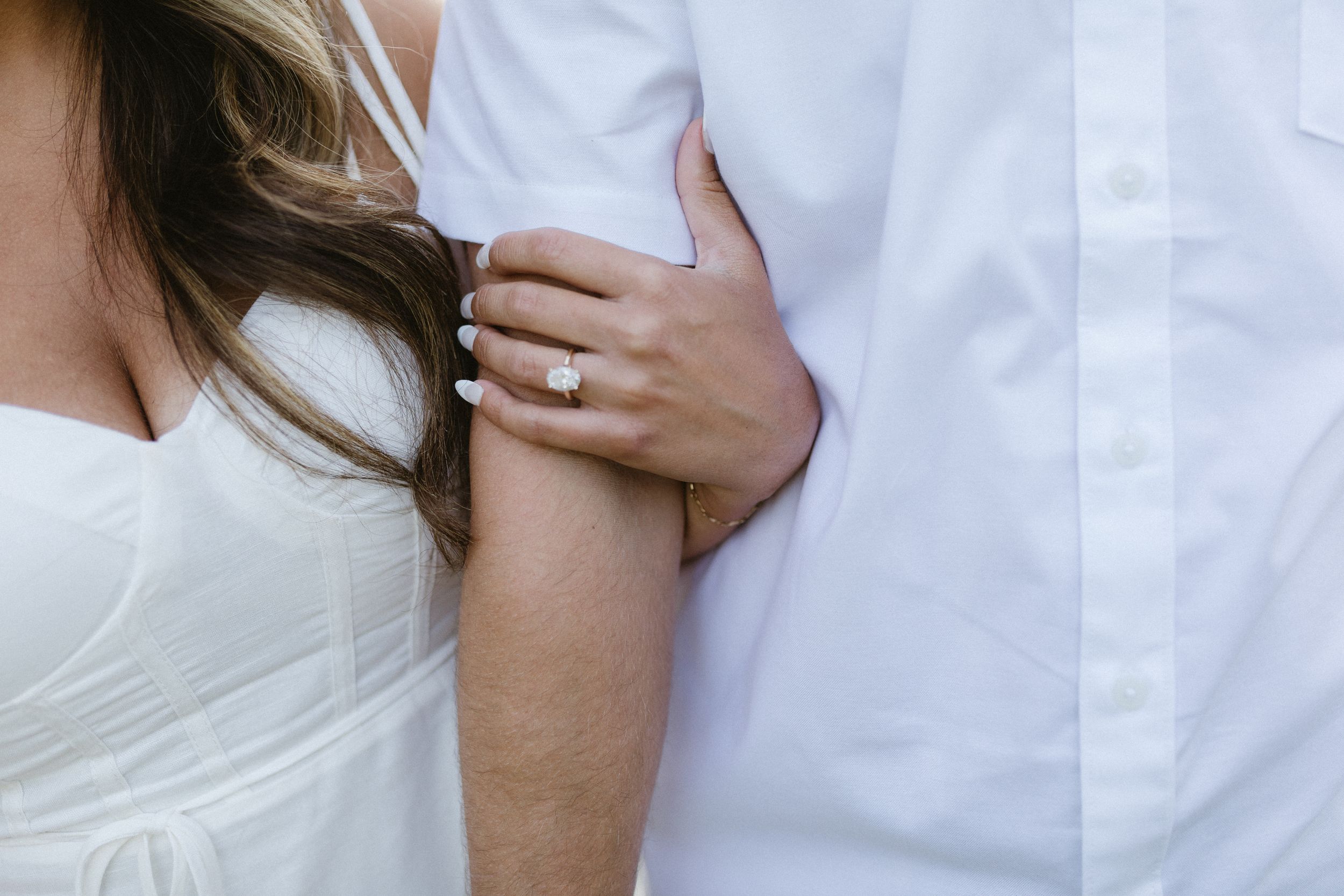 Close-up detail of hands and ring showing intimate moment between couple in white attire.