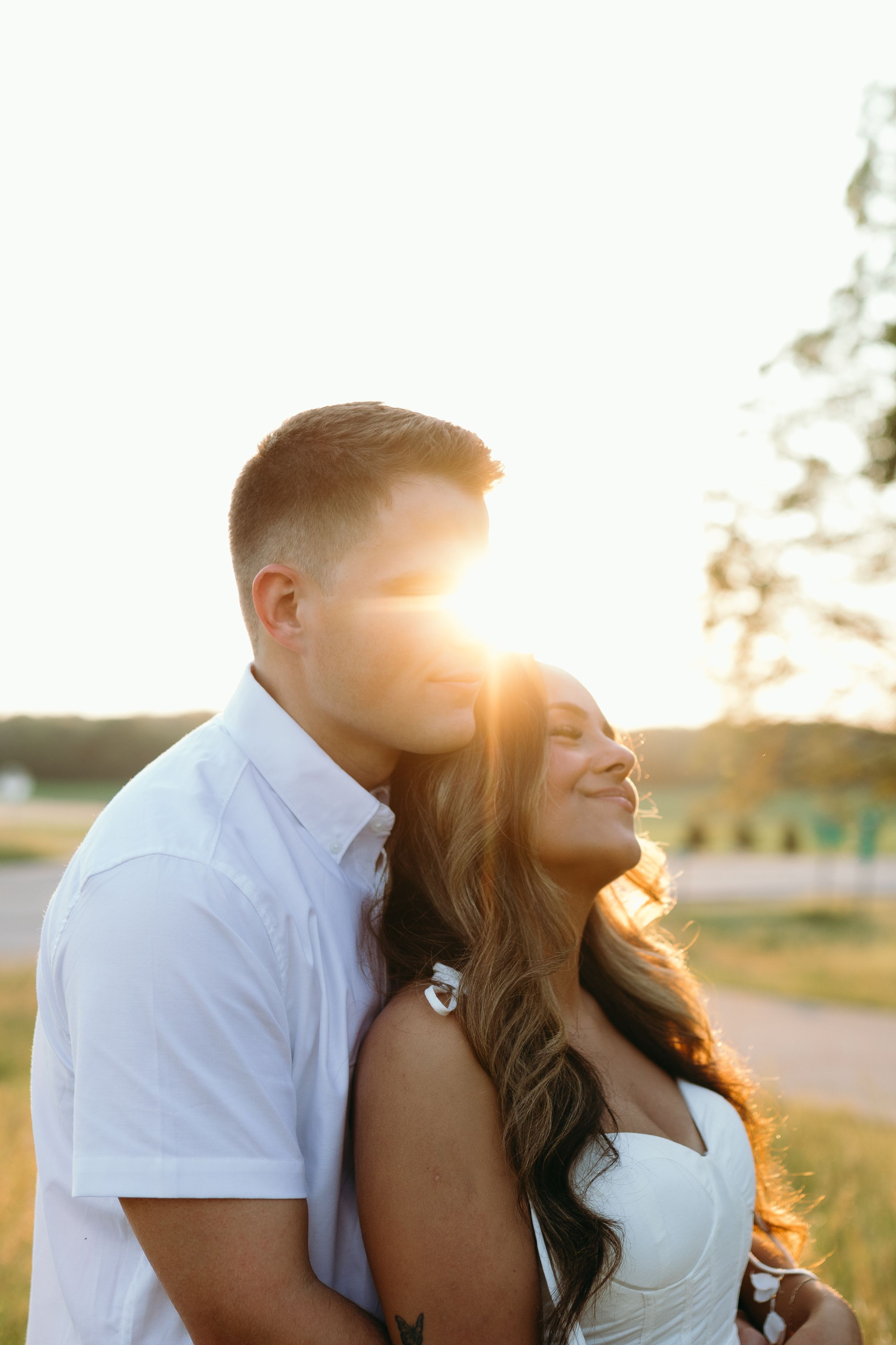Couple embraces in golden sunset light against a rural backdrop with tall grass.