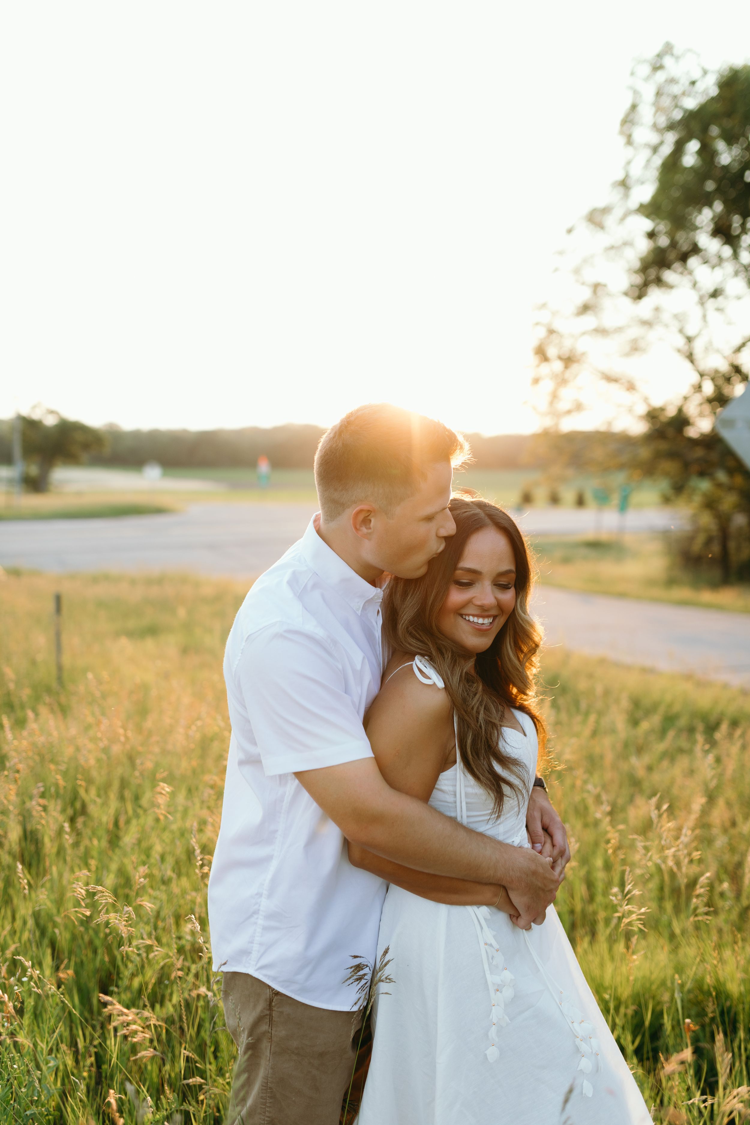 Romantic couple hugging in a field during sunset golden hour.