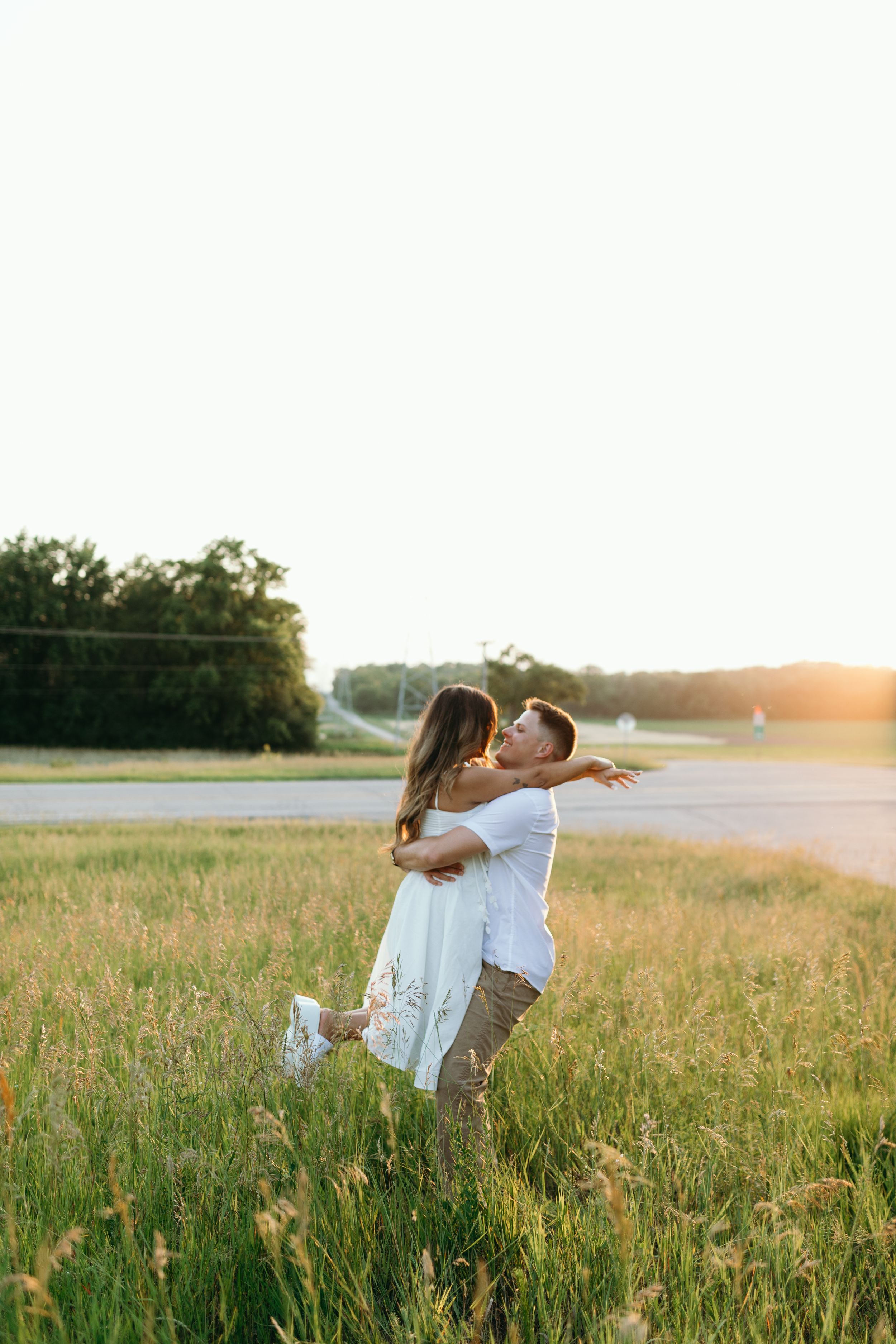 Joyful couple spins together in a sunlit meadow at dusk.