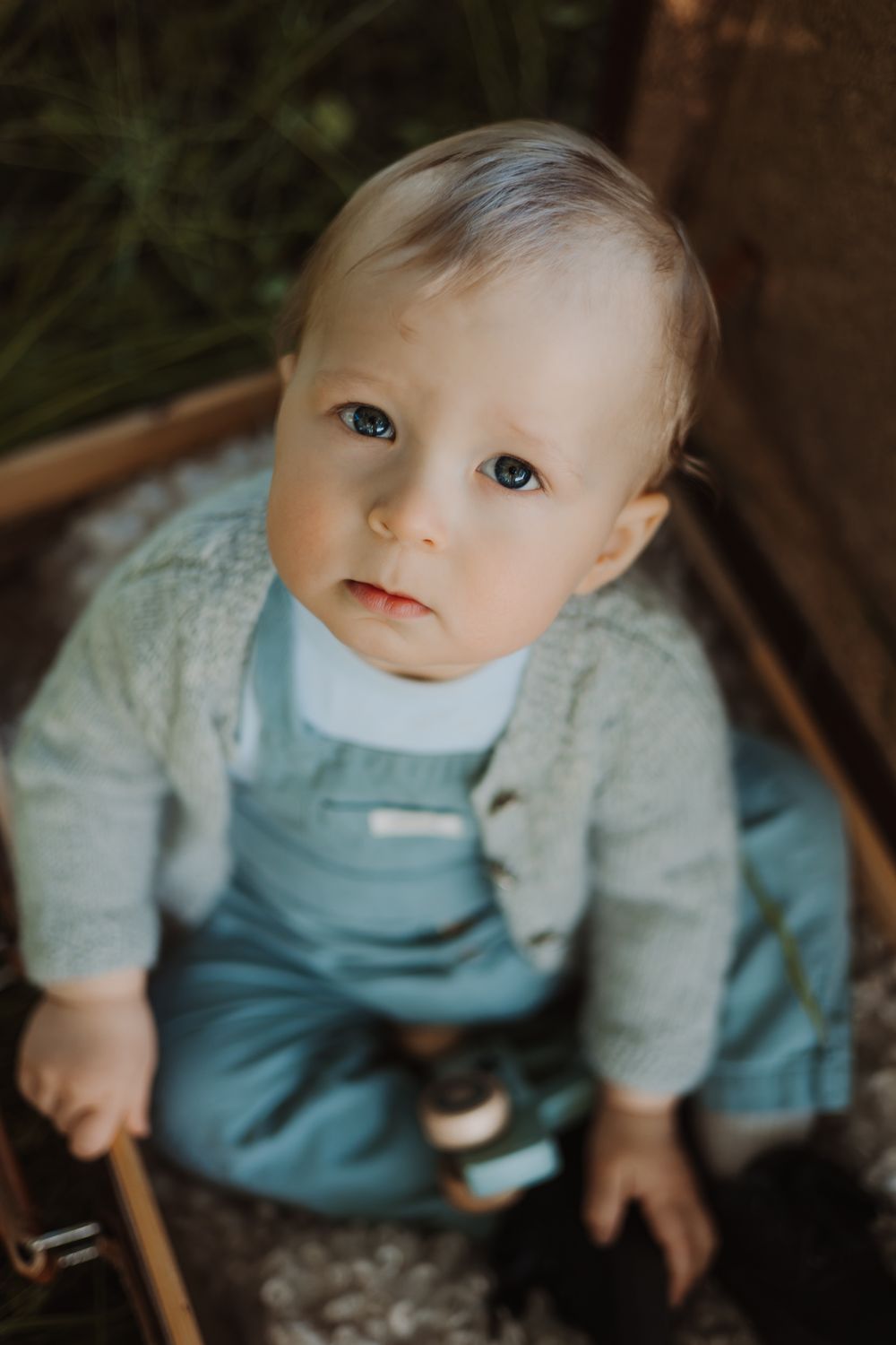 Baby doll wearing blue and gray outfit sitting in wooden chair.