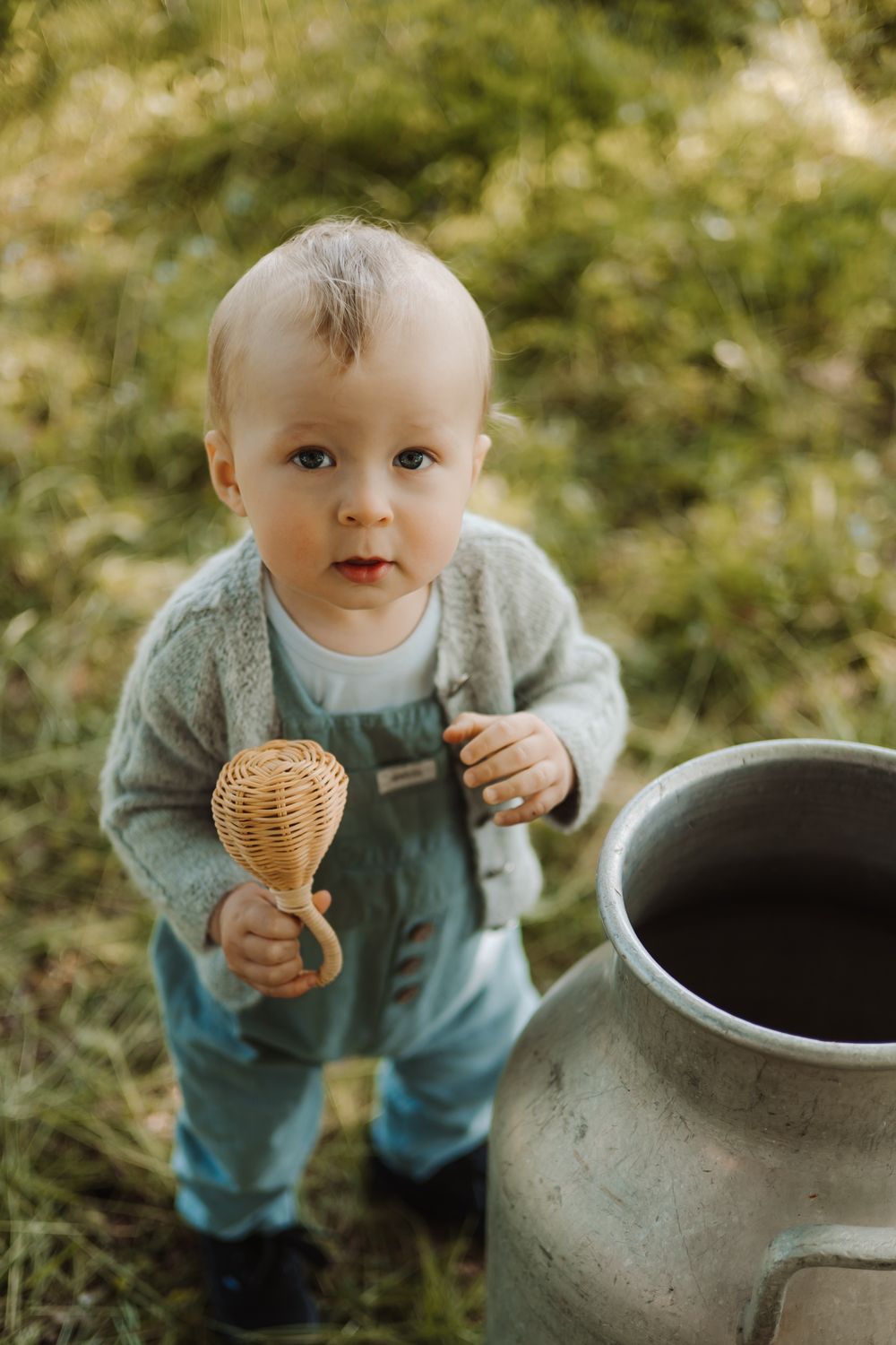 Baby doll in blue overalls standing near large pottery vase outdoors.