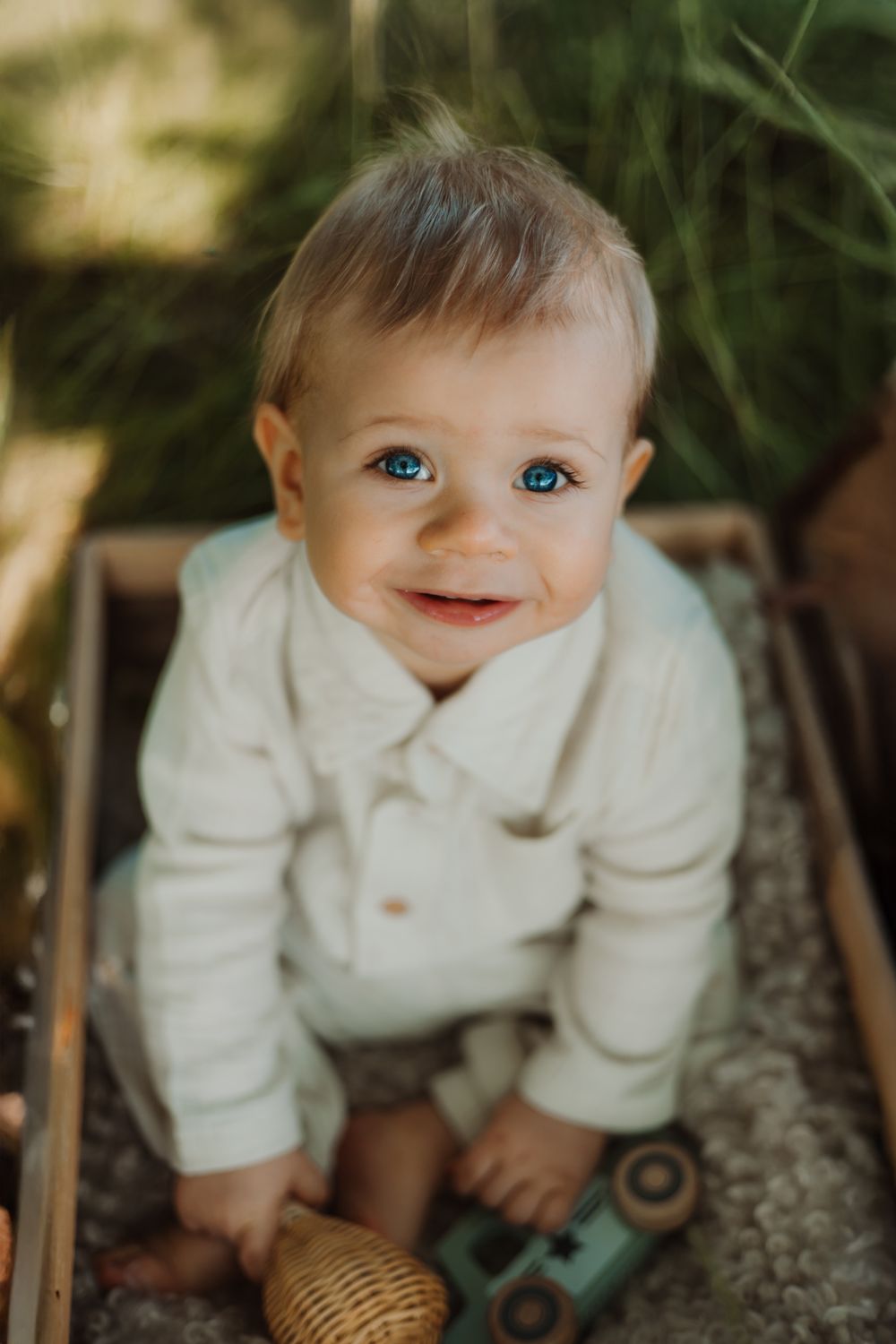 Baby doll in white clothing smiling at camera in outdoor setting.