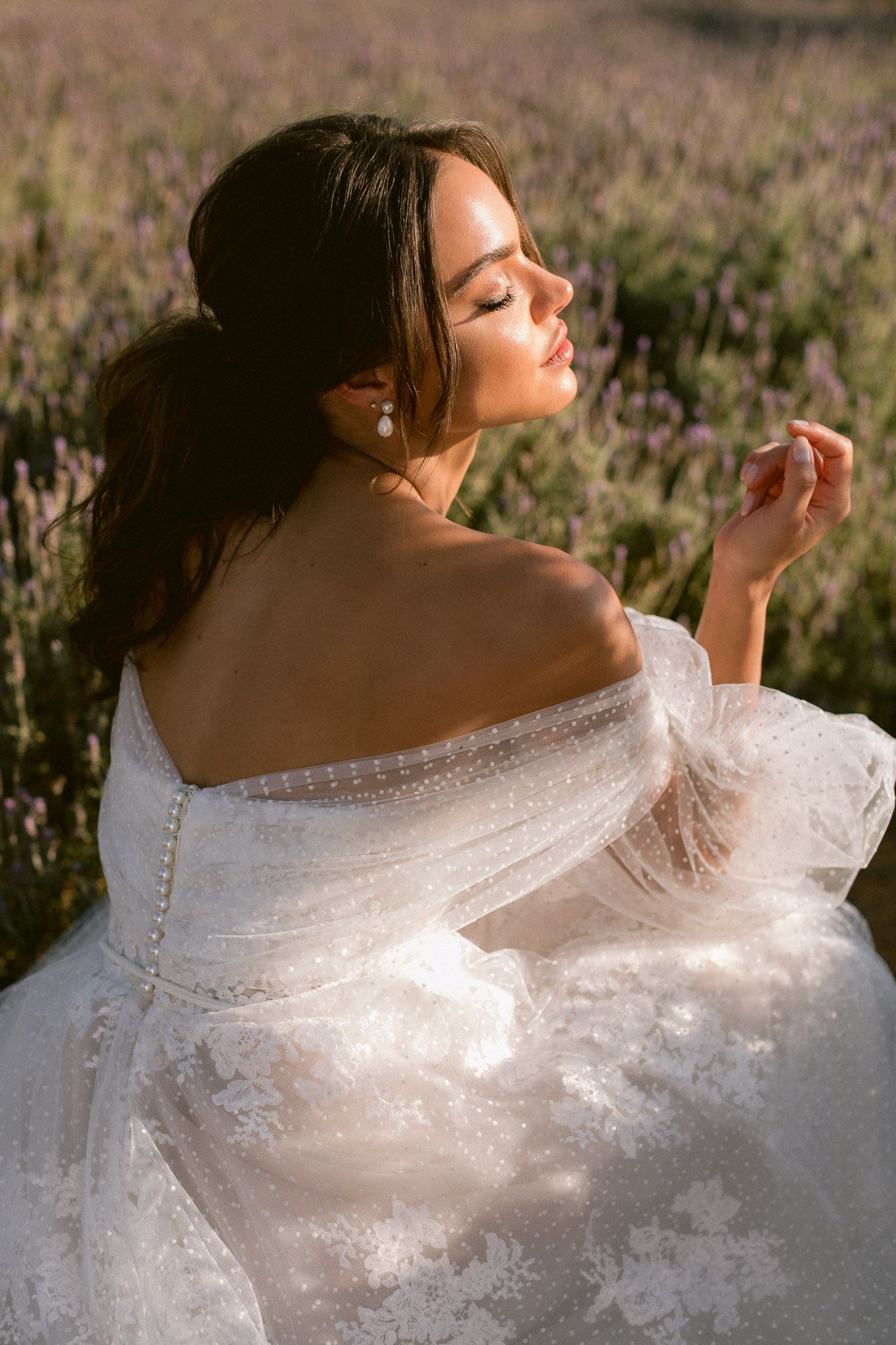 Bride in white dress and straw hat standing in green countryside field.