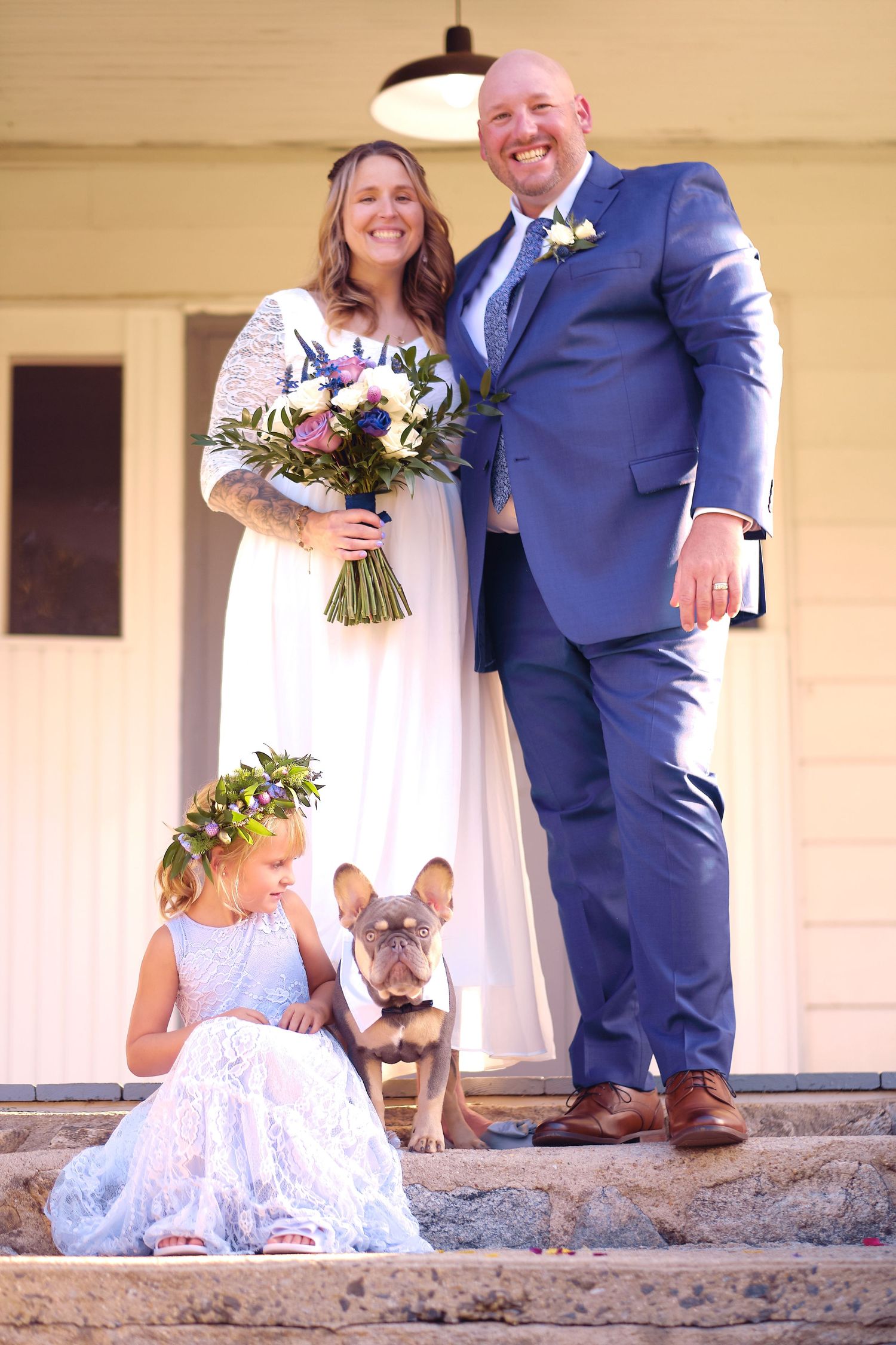 Newlyweds pose for romantic wedding photos on stone steps with a small dog in matching white.