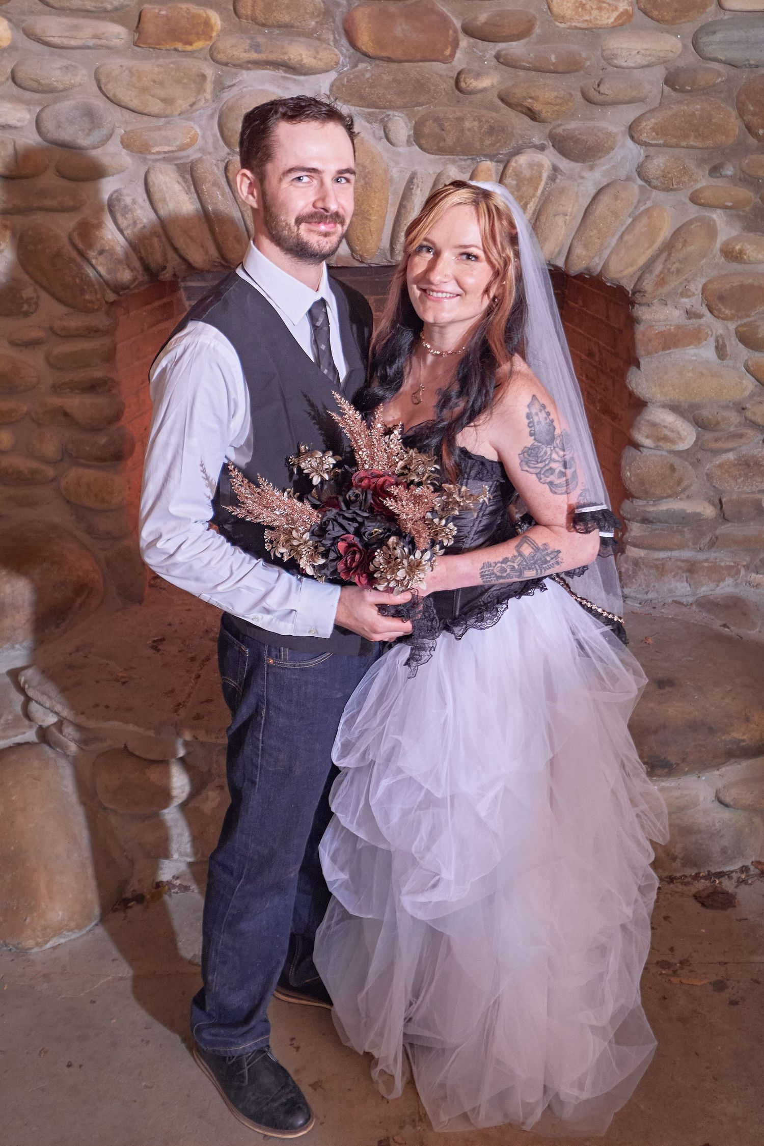 A couple in wedding attire poses playfully in a rustic stone room during their special day celebration.