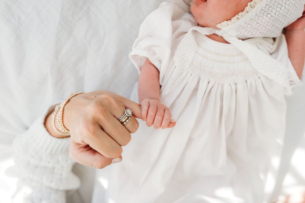 Close-up of hands holding a baby wearing a delicate white dress in New Haven, CT.